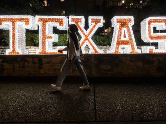 lighted letters that spell TEXAS along a ledge with a person walking in front