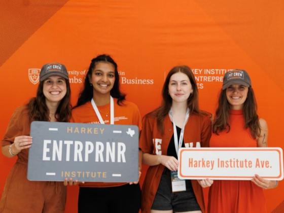 students in front of a burnt orange background holding signs that say entrepreneur