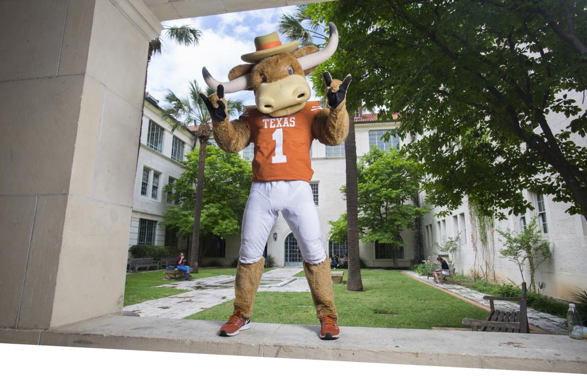 Hook 'em mascot standing on a short wall doing hook 'em hand sign