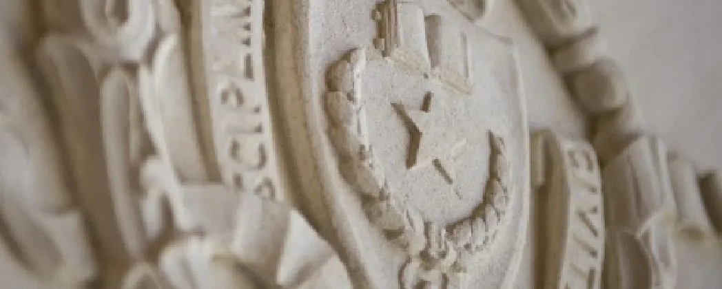 Close up of UT Austin's campus seal carved into cream colored stone.