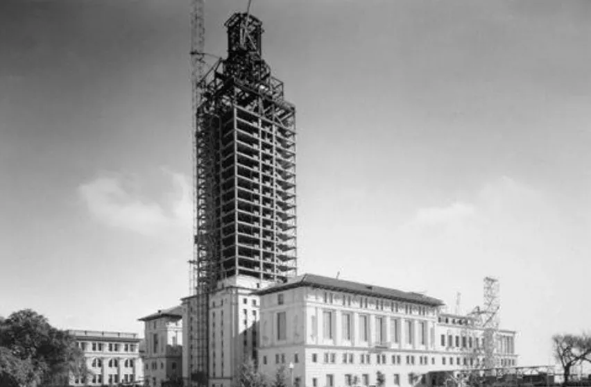 A black and white show of UT Tower under construction, there is scaffolding going up the entirety of the tower.