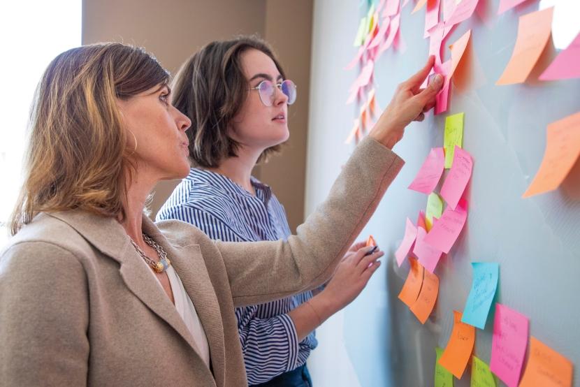 Two people working at a board doing a card sorting activity with Post-It notes