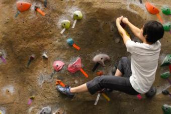 A man climbs on a brown rock wall at UT. His hands hold onto one rock while his foot stretches out to reach the rocks below him.