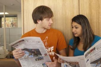 Two students sit next to each other and talk while holding The Daily Texan newspapers.