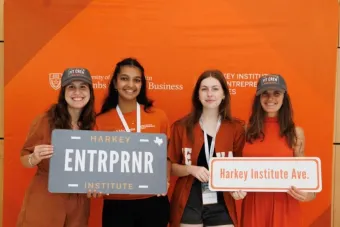 Four students posing with signs in front of a burnt orange background