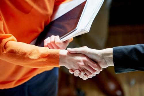 A handshake is exchanged between two professionally dressed individuals wearing orange and black respectively.