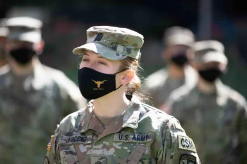 UT Army ROTC students stand in camo uniforms. The central girl is in focus and wearing a black mask with a UT logo.